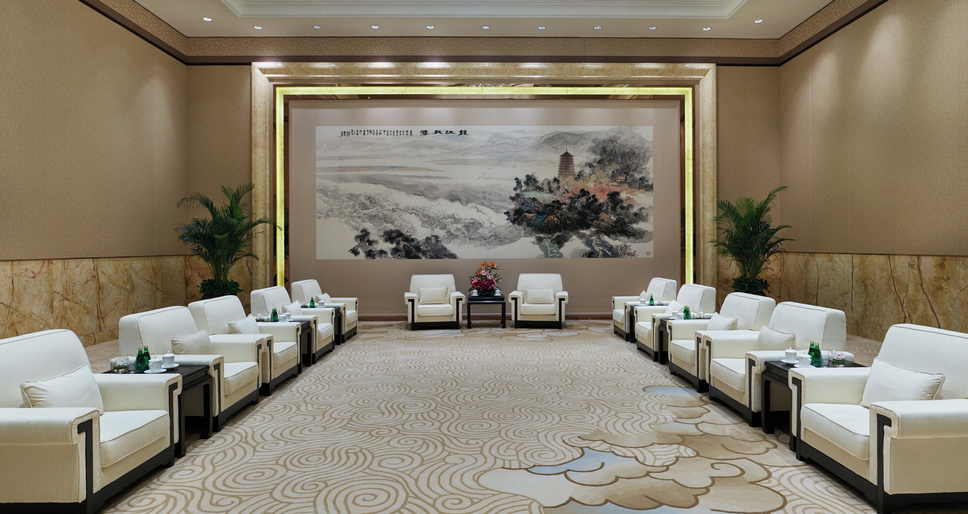 A conference room with a large screen displaying a painting, arranged seating, and a patterned carpet.