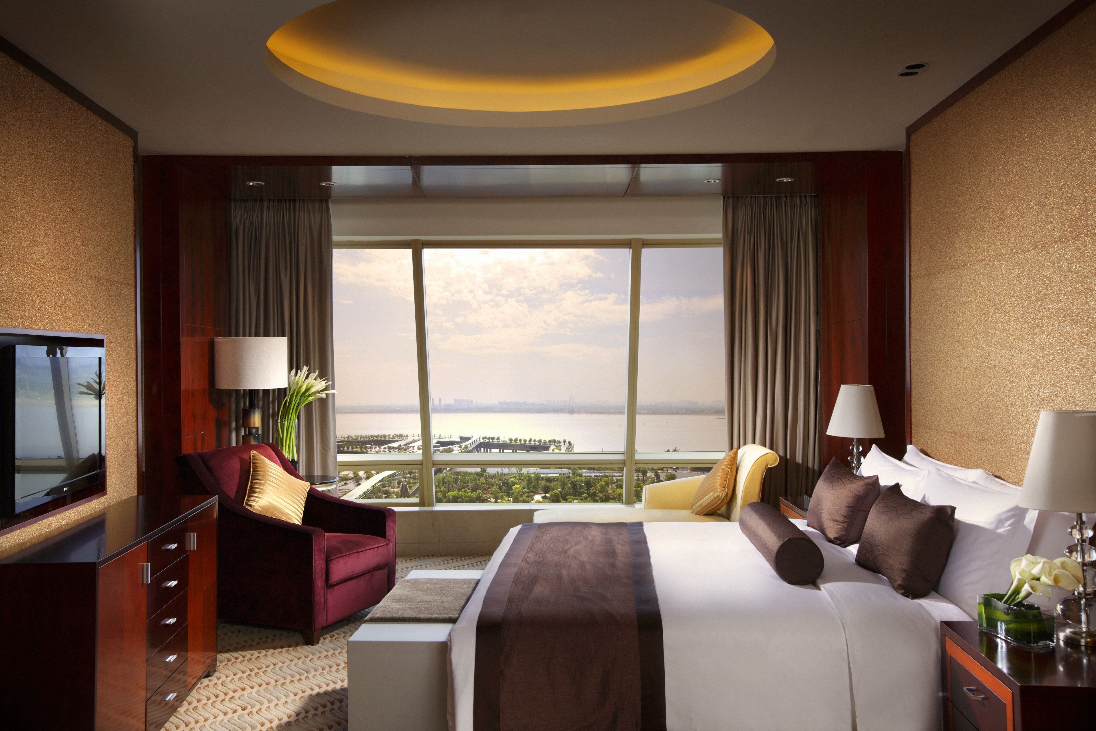 A hotel room with a large bed, a TV, a desk, and a view of a body of water.