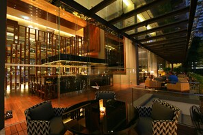 A modern indoor-outdoor dining area with glass walls, wooden flooring, and a bar. - Hansar Bangkok Hotel (Bangkok)