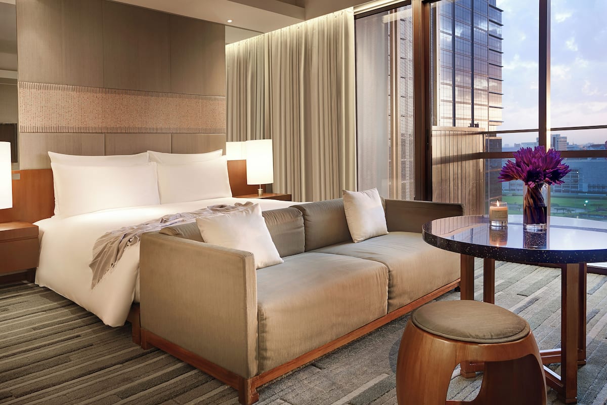 A hotel room with a bed, sofa, and a small table with a candle and flowers.