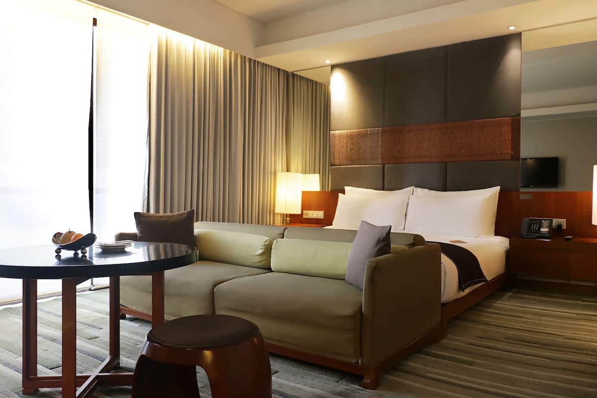 A hotel room with a bed, a sofa, a table, and a TV.