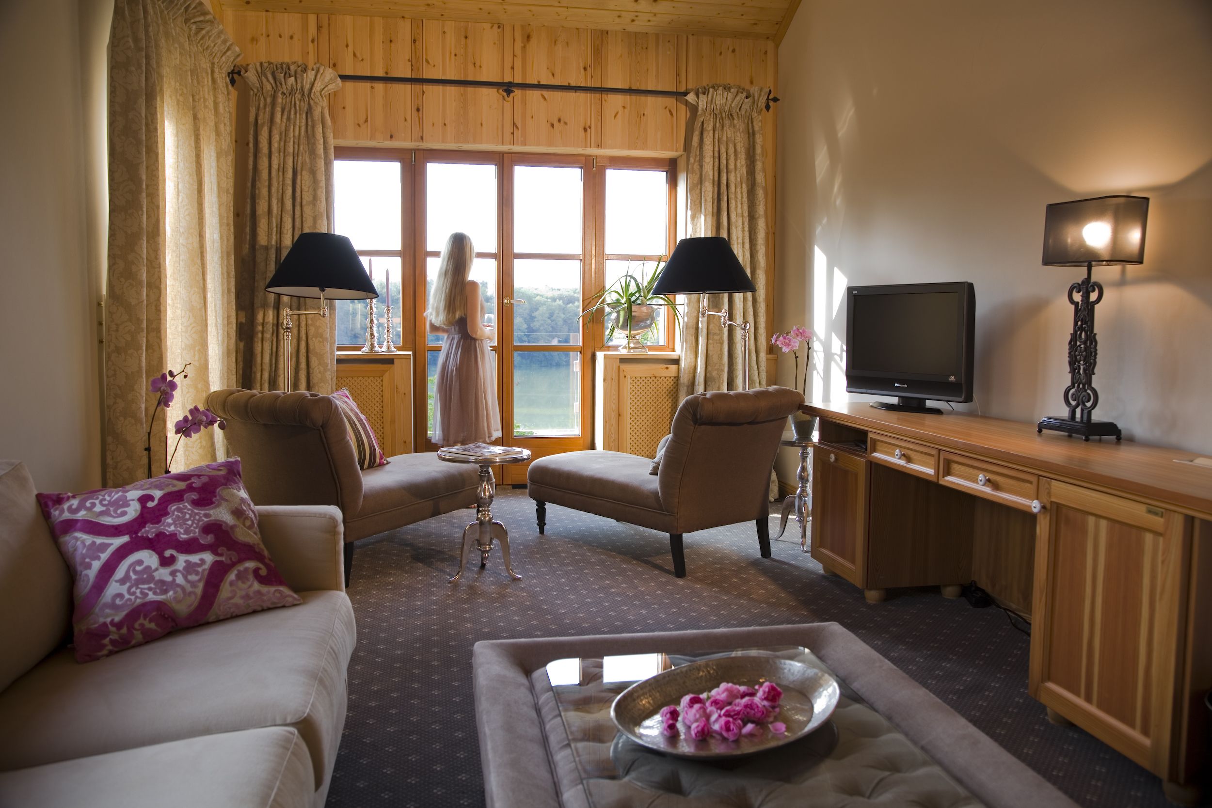 Una sala de estar acogedora con un sofá, sillones, una mesa de centro con flores, un televisor y un escritorio con lámpara.