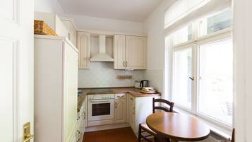 A compact kitchen with white cabinets, a stove, and a window.