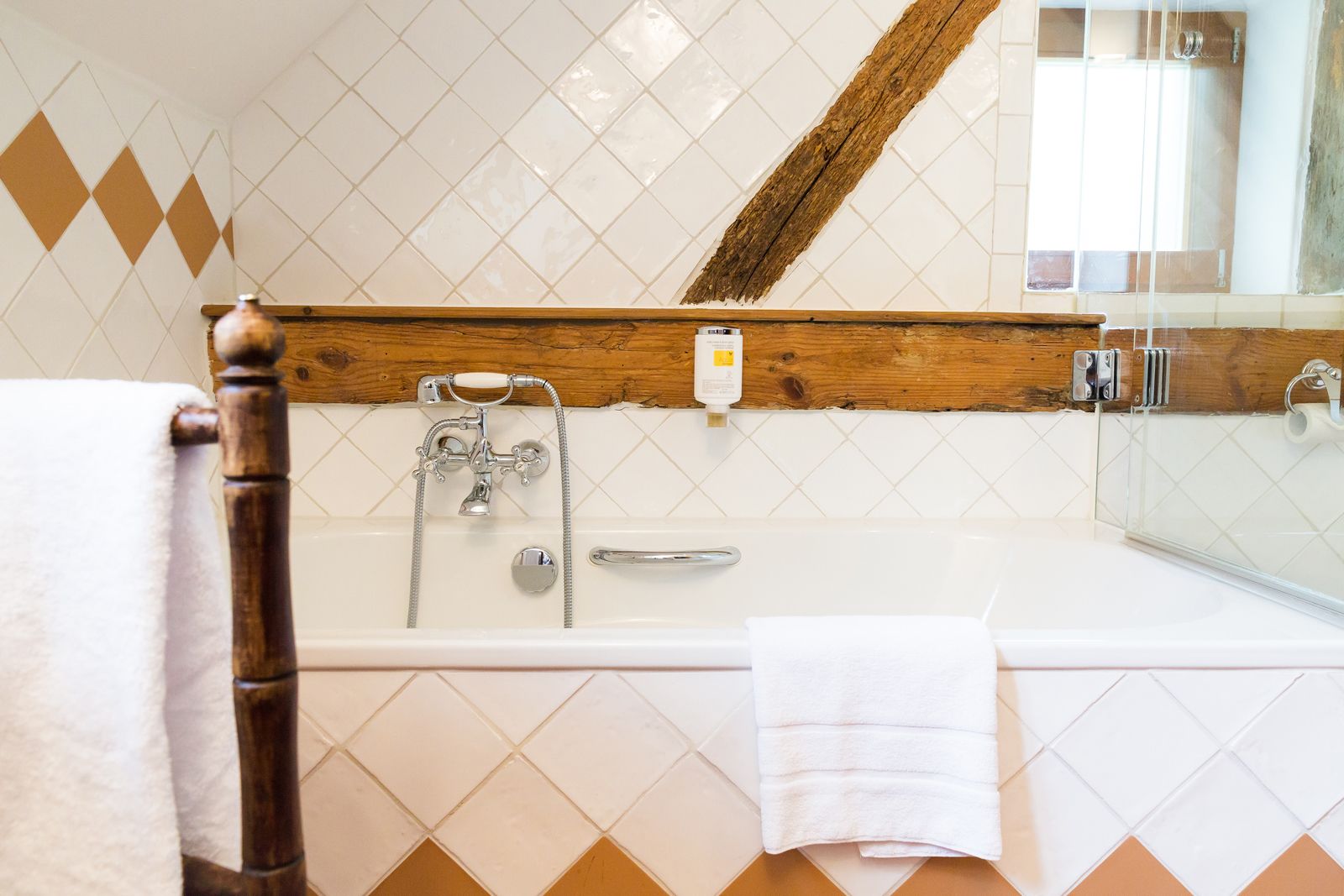 A bathroom with a bathtub, a wooden-framed mirror, and a white tiled wall.