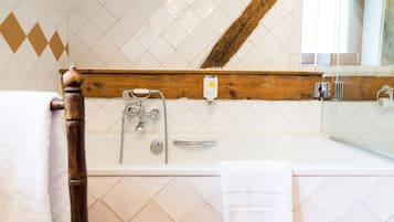 A bathroom with a bathtub, a wooden-framed mirror, and a white tiled wall.