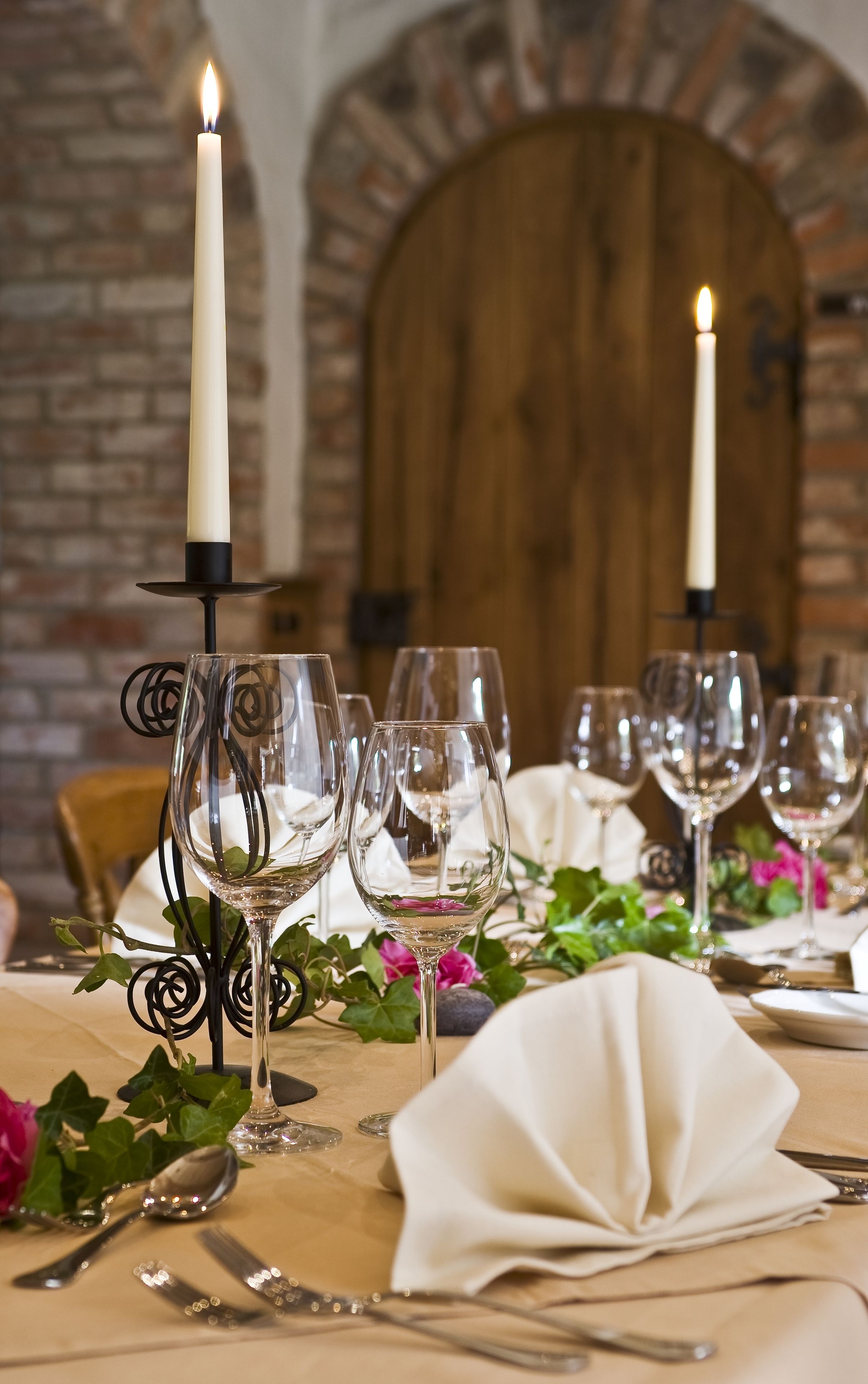 A table set for a meal with candles, wine glasses, and a rustic brick wall in the background.