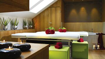 Un spa moderno con techo de madera, una camilla de masaje, otomanas verdes y velas.