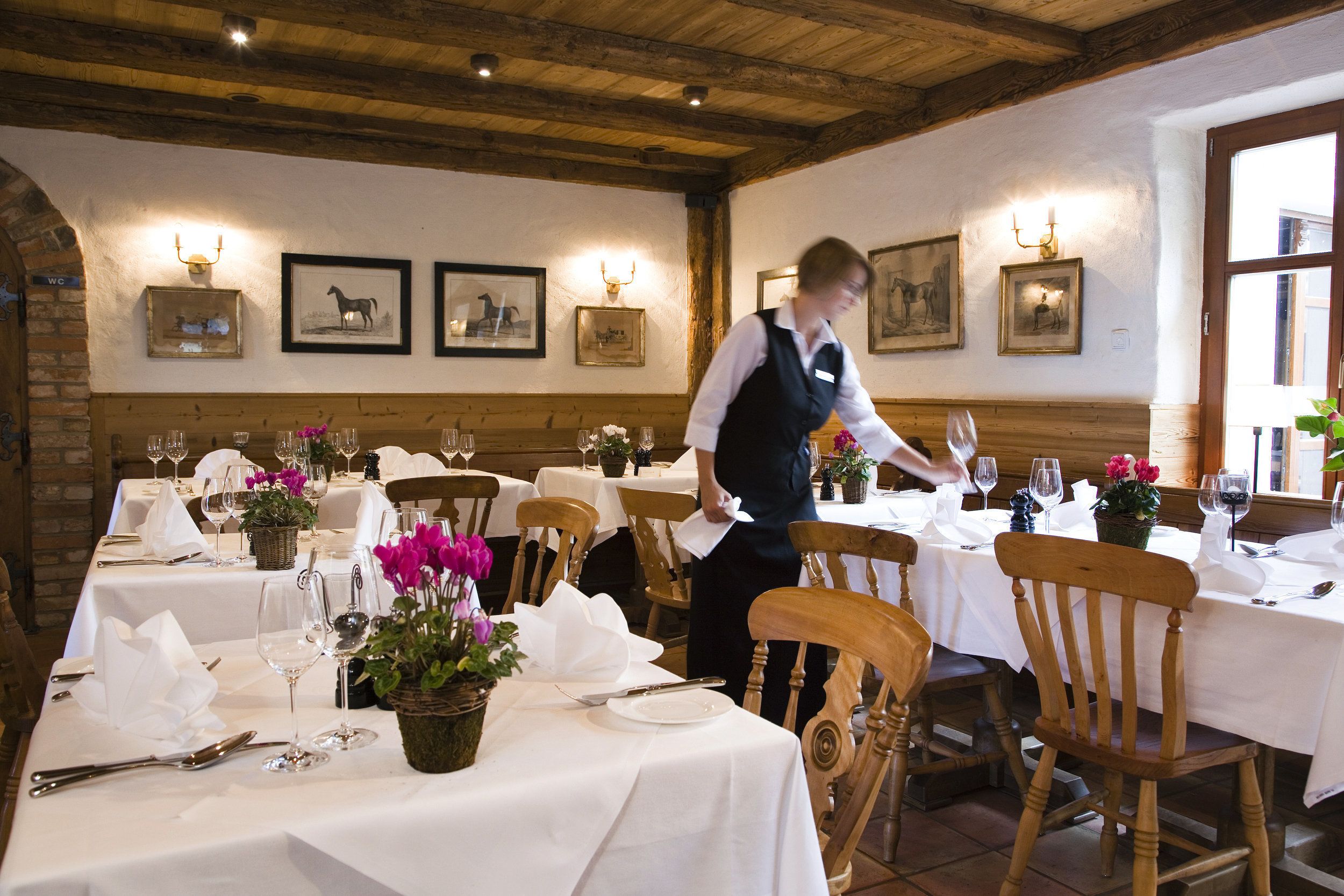 A restaurant with wooden beams, white tablecloths, and framed pictures on the walls.