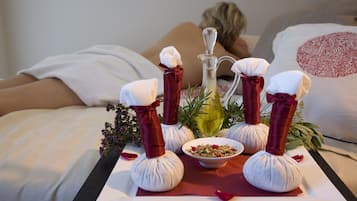 En massageopstilling med håndklæder, en skål med urter og en flaske olie på en bakke.