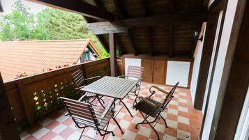A covered patio with a checkered floor, wooden furniture, and a view of a house with a red roof.