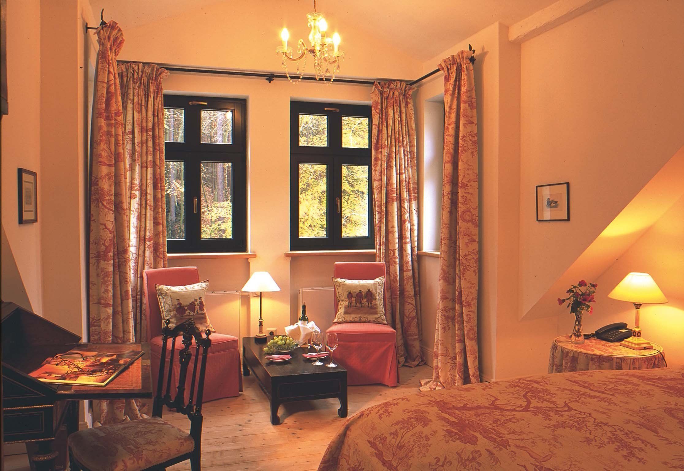 A cozy room with a piano, a red armchair, a small table with a lamp, and a bed with a floral bedspread.