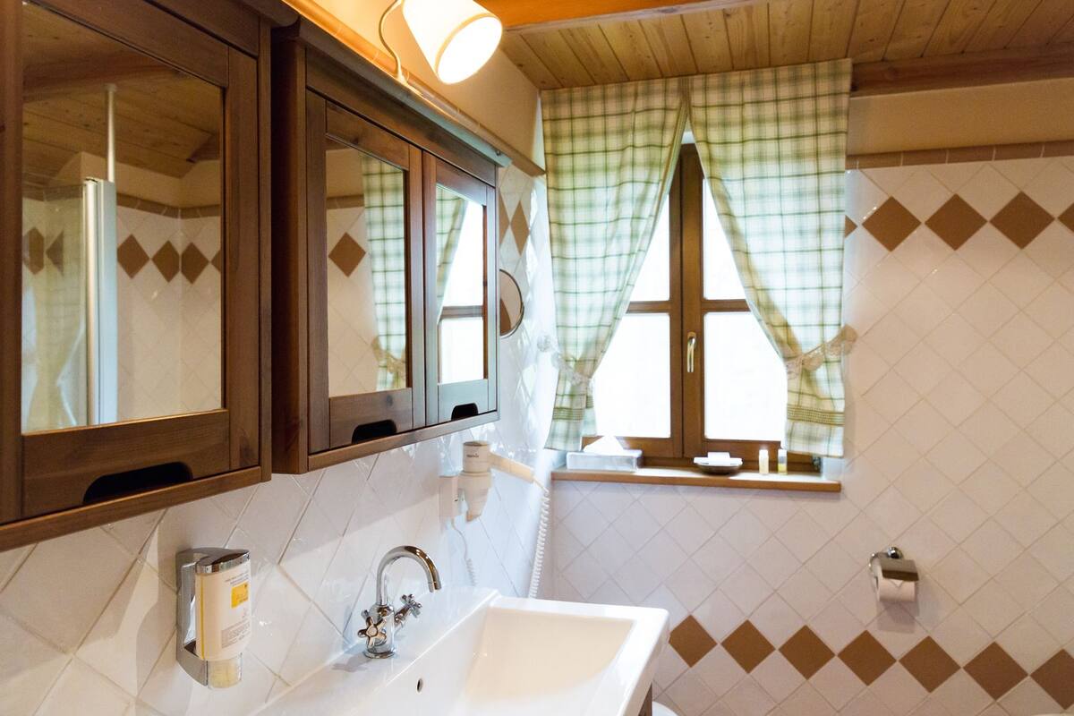 Une salle de bain avec un lavabo blanc, un miroir et une fenêtre ornée de rideaux à carreaux.