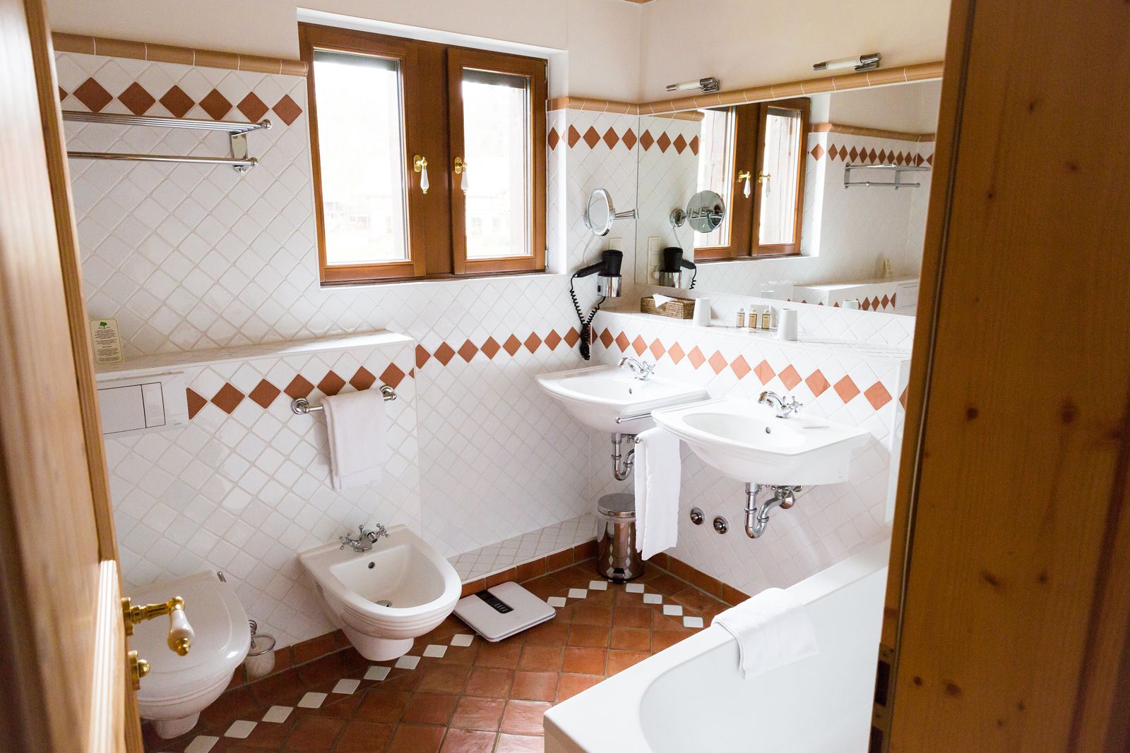 A bathroom with two sinks, a bidet, a toilet, a bathtub, and a window with wooden frames.