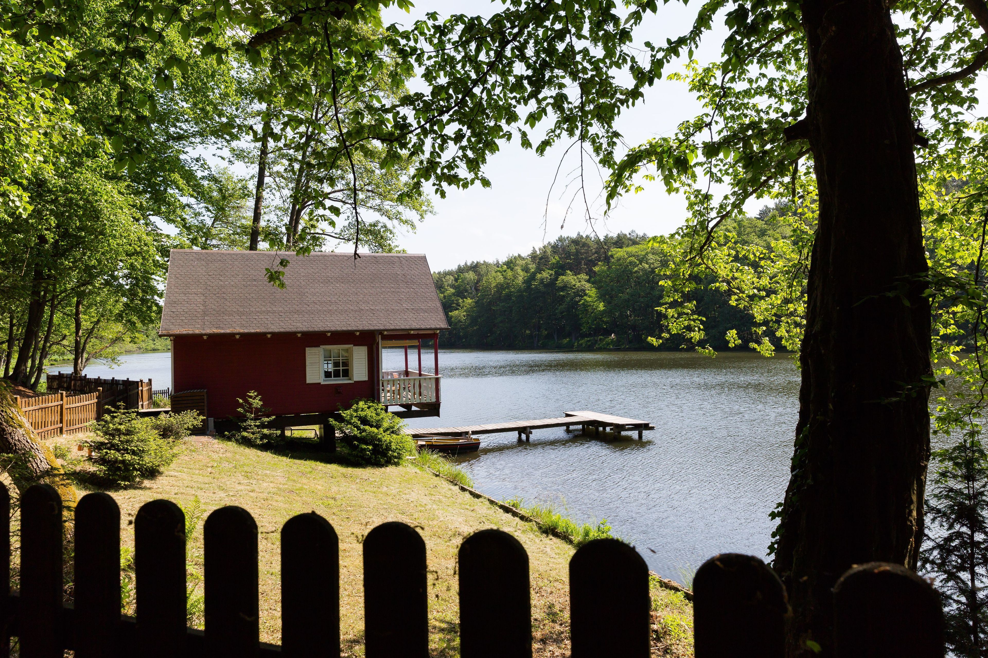 Una cabaña junto a un lago con un muelle, rodeada de árboles.