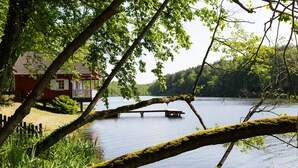 A lakeside cabin with a dock extending into the water, surrounded by lush greenery. - Gut Klostermühle (Briesen)