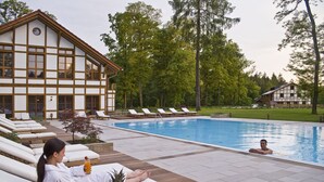 A poolside area with lounge chairs, a wooden deck, and a building with large windows. - Gut Klostermühle (Briesen)
