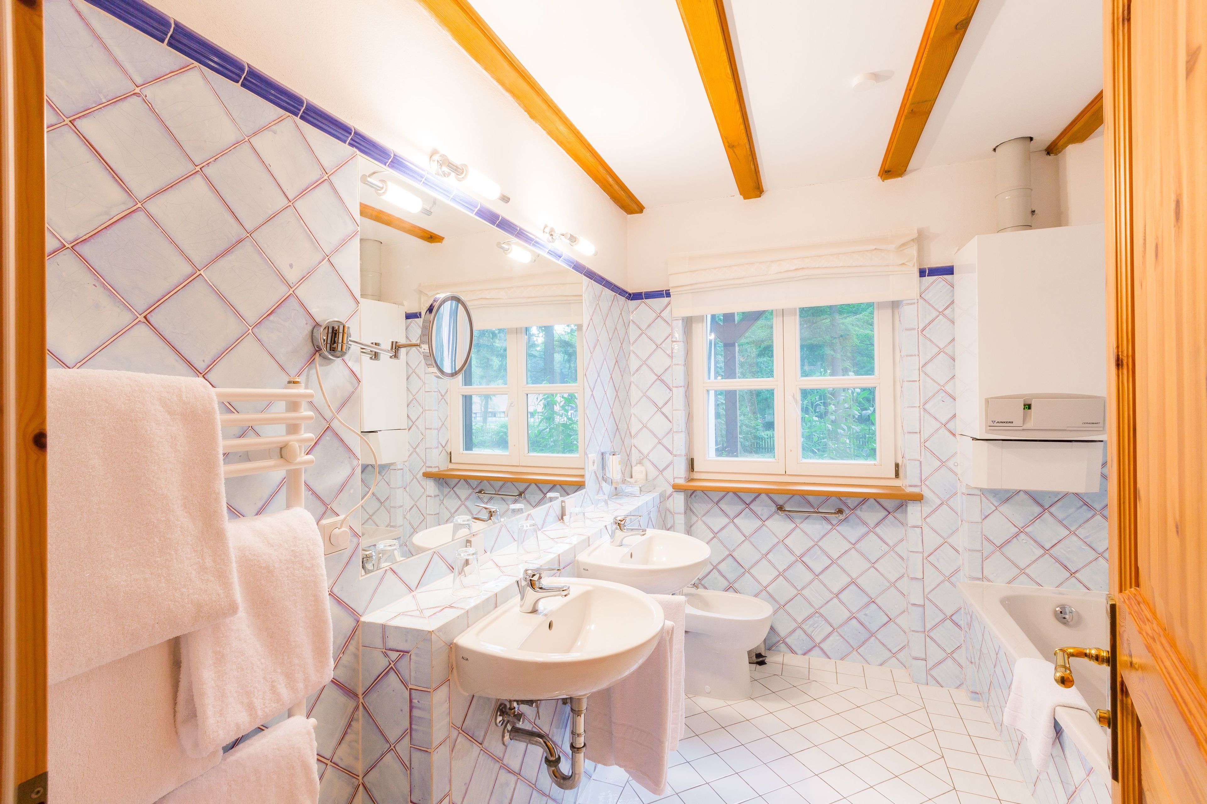 Un bagno con tre lavandini, un bidet e una vasca da bagno. Asciugamani appesi a un porta asciugamani, e una finestra lascia entrare luce naturale.