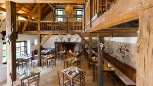A rustic interior with wooden beams, a fireplace, and antler decorations. Tables and chairs are arranged for dining. - Gut Klostermühle (Briesen)