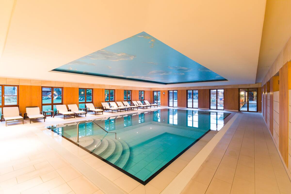 Une grande piscine intérieure dotée de nombreuses chaises longues et ornée d’une fresque au plafond.