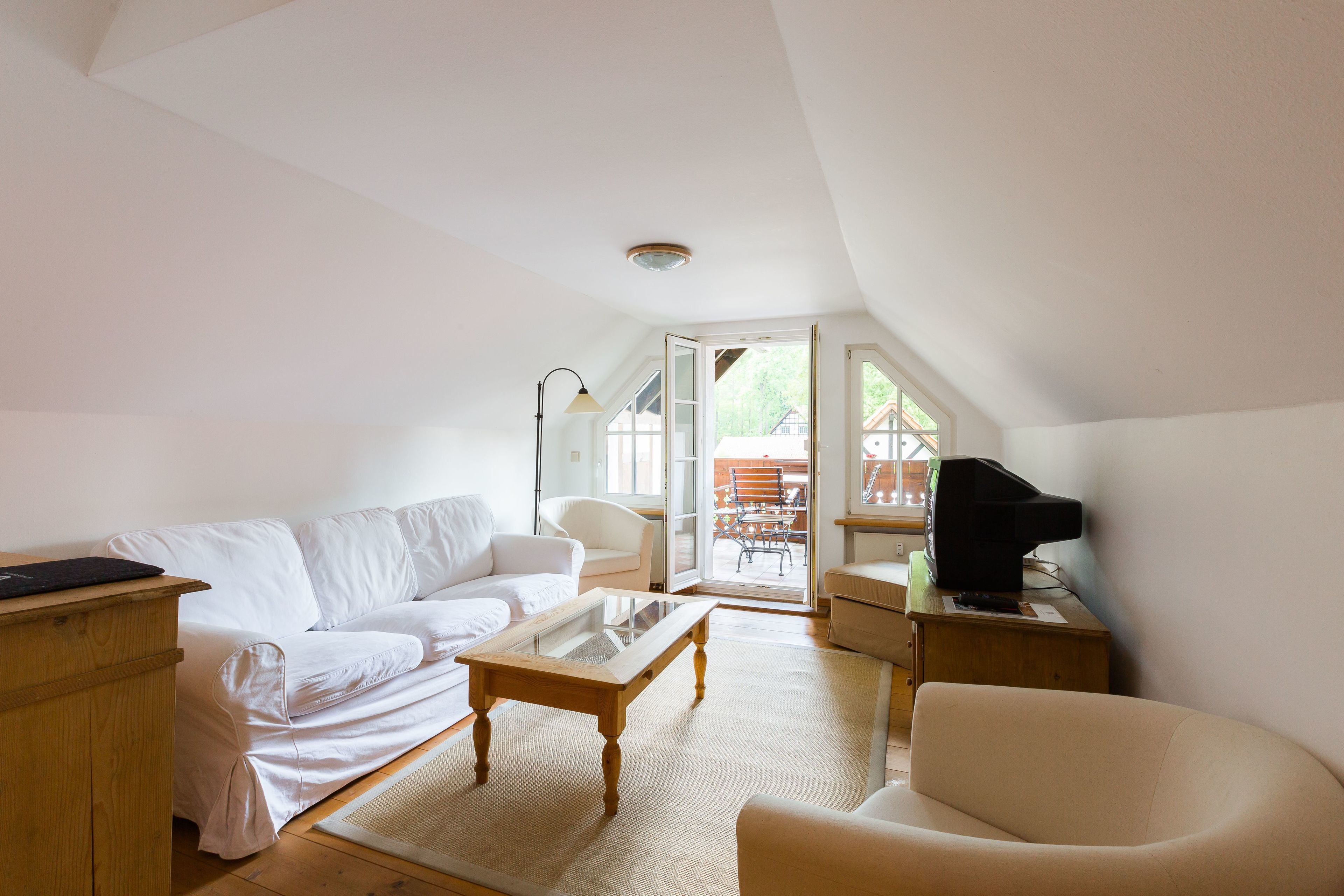 Amplio dormitorio tipo loft con un gran ventanal, un sofá blanco, una mesa de centro de madera y un televisor sobre una mesita auxiliar de madera.