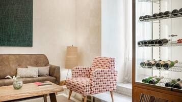 Ein Wohnzimmer mit einem braunen Sofa, einem gemusterten Sessel, einem Weinkühlschrank aus Glas und einem Couchtisch mit Vase und Buch.