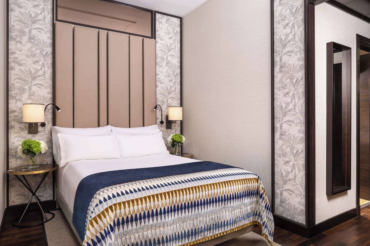 A neatly made bed with a patterned bedspread, two bedside lamps, and a small table with a vase of flowers.