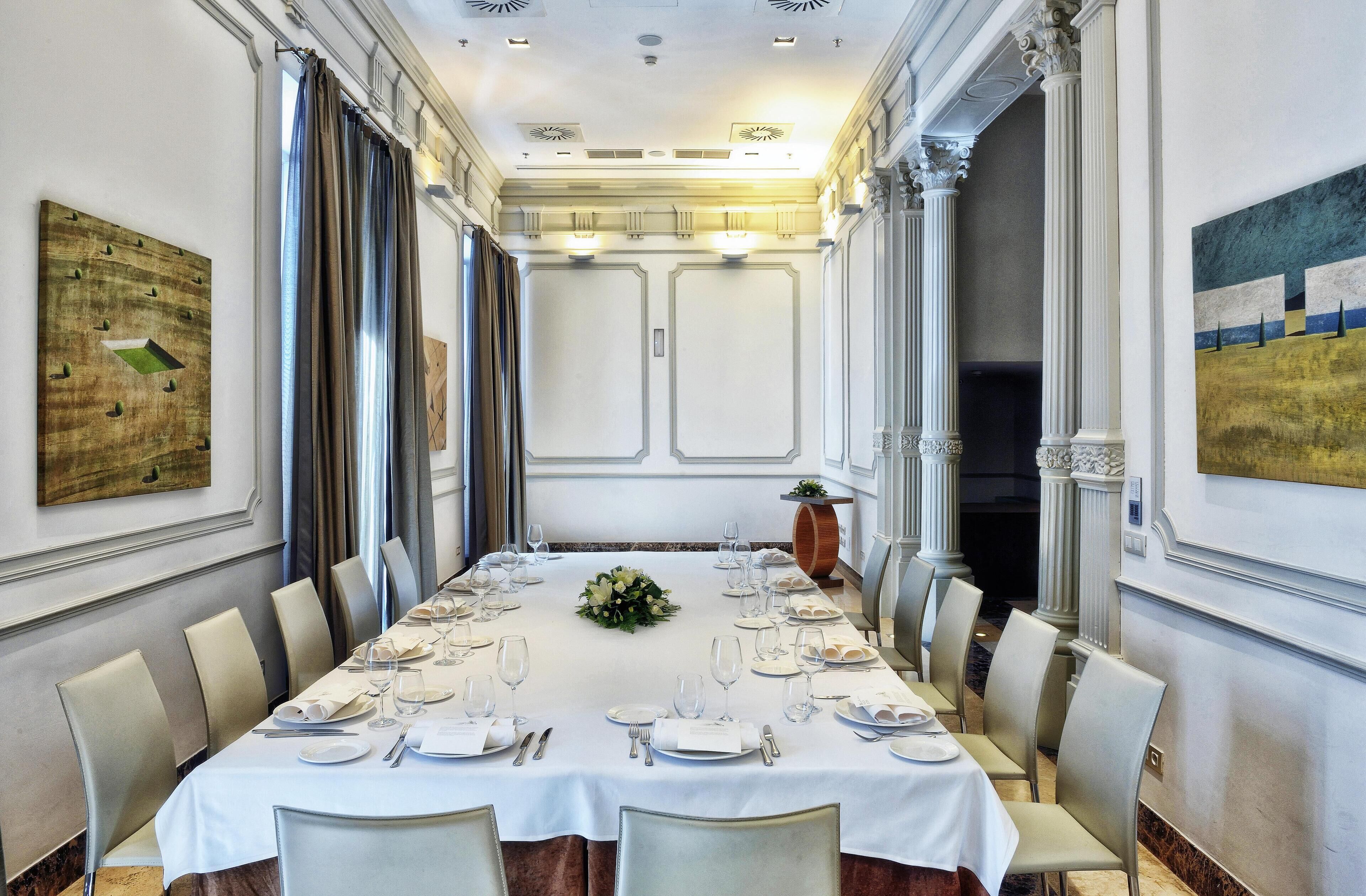 A formal dining room with a long table set for a meal, flanked by tall columns and large windows.