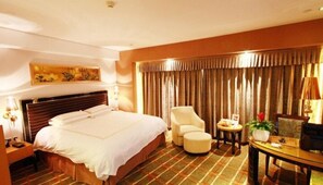 A hotel room with a large bed, a chair, a small table, and a desk. - Jinding Hotel (Wenzhou)