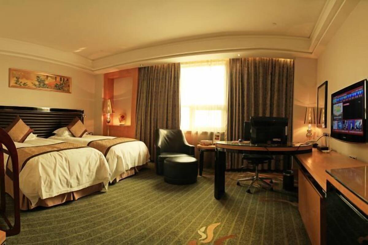 Hotellihuone, jossa on kaksi sänkyä, työpöytä, televisio ja ikkuna, jossa on verhot.