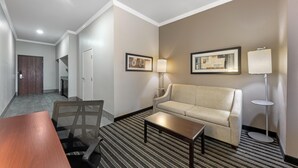 A hotel room with a sofa, a coffee table, a desk with a chair, a lamp, and framed artwork on the walls. - Best Western Plus Austin Airport Inn & Suites (Austin)