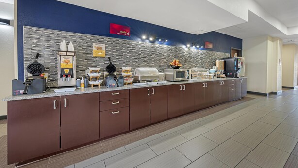 A modern kitchen area with a long counter, various appliances, and a tiled backsplash. - Best Western Plus Austin Airport Inn & Suites (Austin)