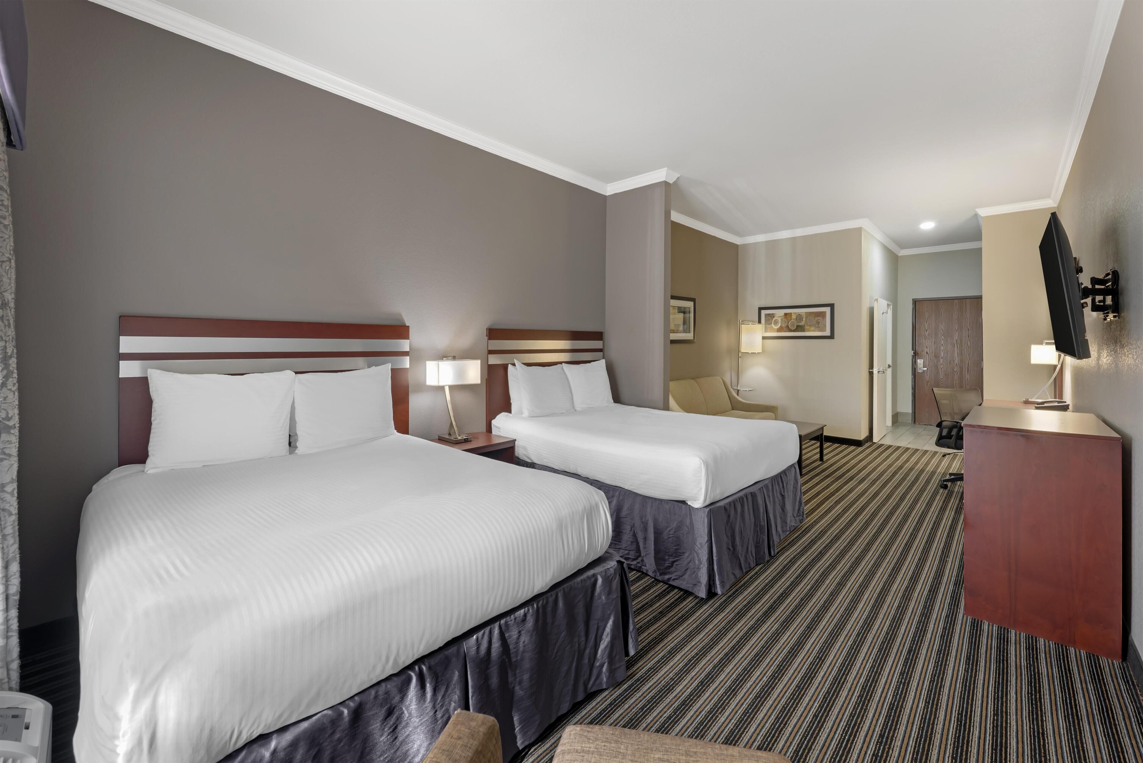 Quarto de hotel com duas camas, uma escrivaninha, uma televisão e um banheiro visível ao fundo.