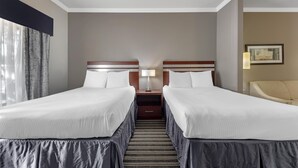 A hotel room with two beds, a nightstand with a lamp, a chair, and a framed picture on the wall. - Best Western Plus Austin Airport Inn & Suites (Austin)