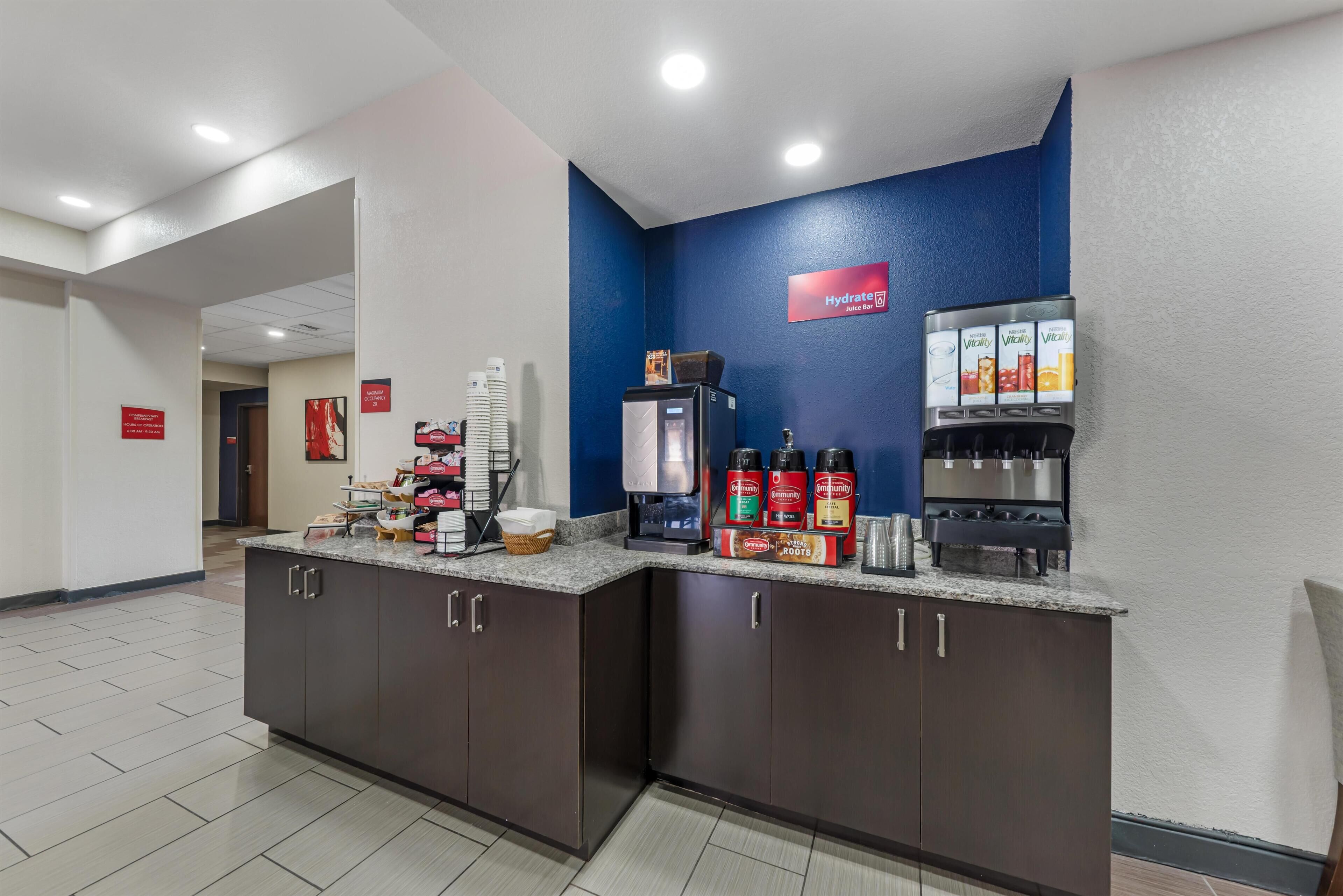 A hotel reception area with a coffee station, a refrigerator, and a sign for 'Hydrate'.