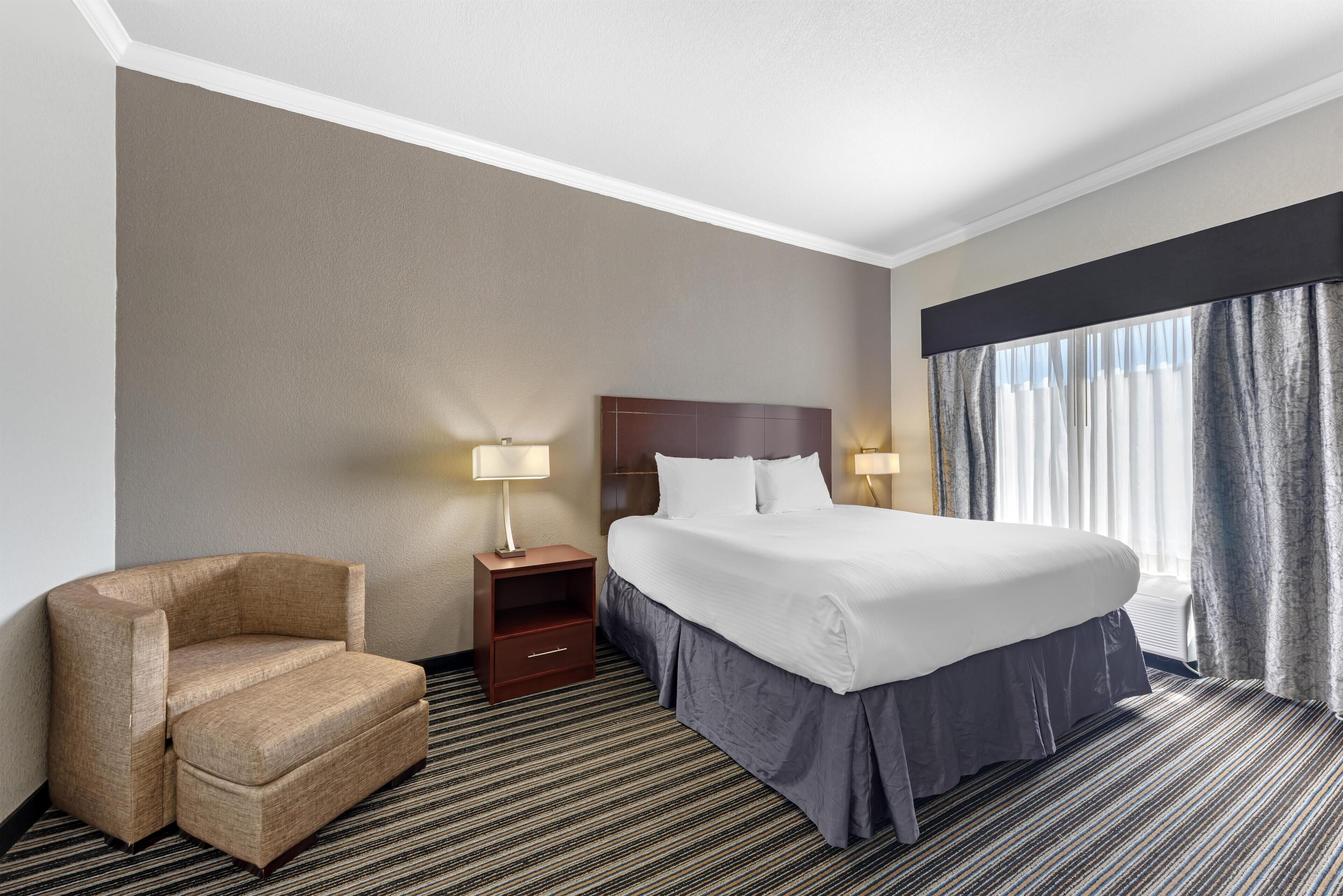 A hotel room with a bed, a chair, a nightstand, and a window with curtains.