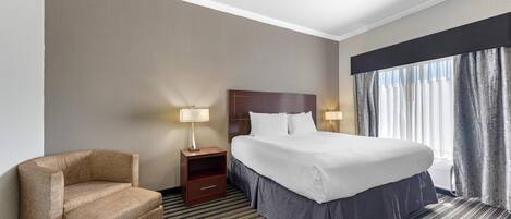 A hotel room with a bed, a chair, a nightstand, and a window with curtains.