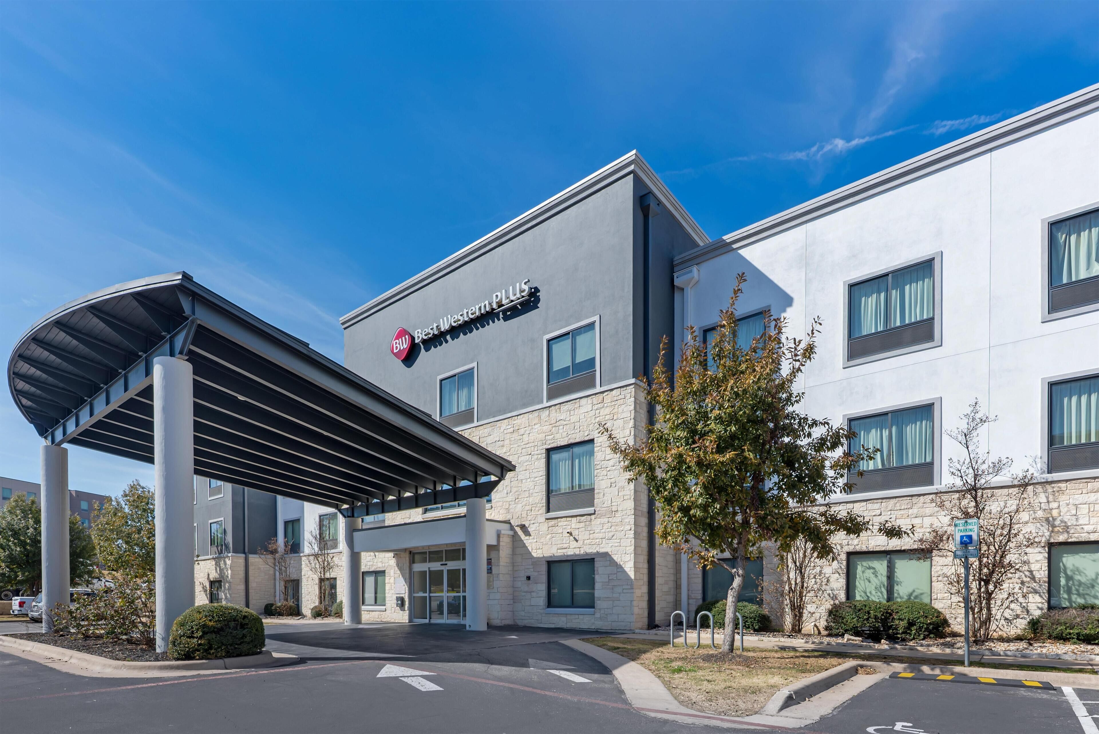 A modern building with a covered entrance, a sign reading "Best Western PLUS," and a parking area with marked spaces.