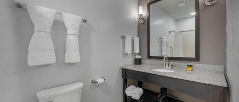 A modern bathroom with a toilet, sink, and mirror. There are towels hanging on the wall and a shelf under the sink.