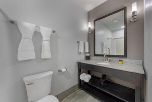 A modern bathroom with a toilet, sink, and mirror. There are towels hanging on the wall and a shelf under the sink.