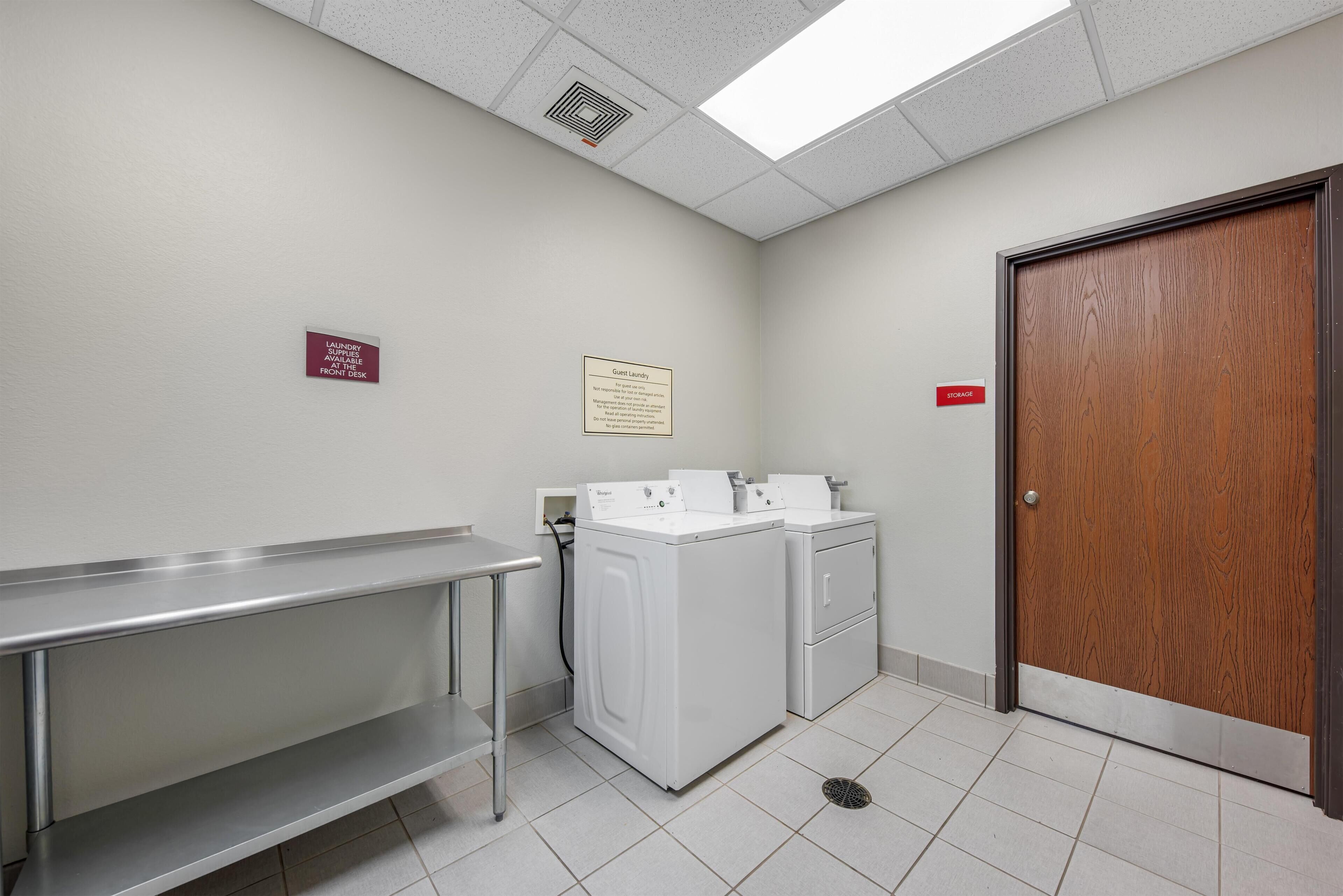 A laundry room with a washing machine, dryer, and a sink. There is a sign indicating guest laundry availability.