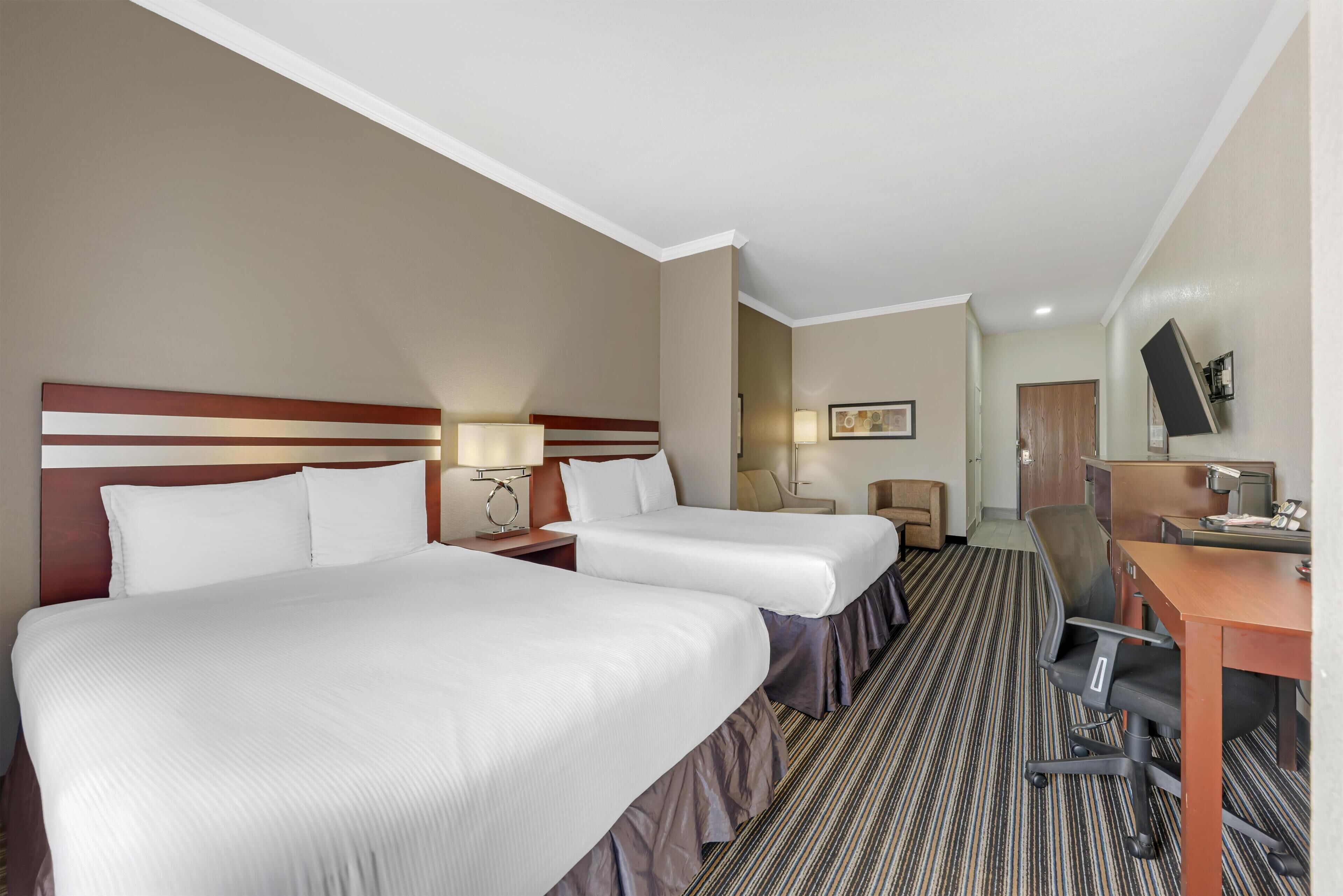 A hotel room with two beds, a desk, a chair, a TV, and a door.