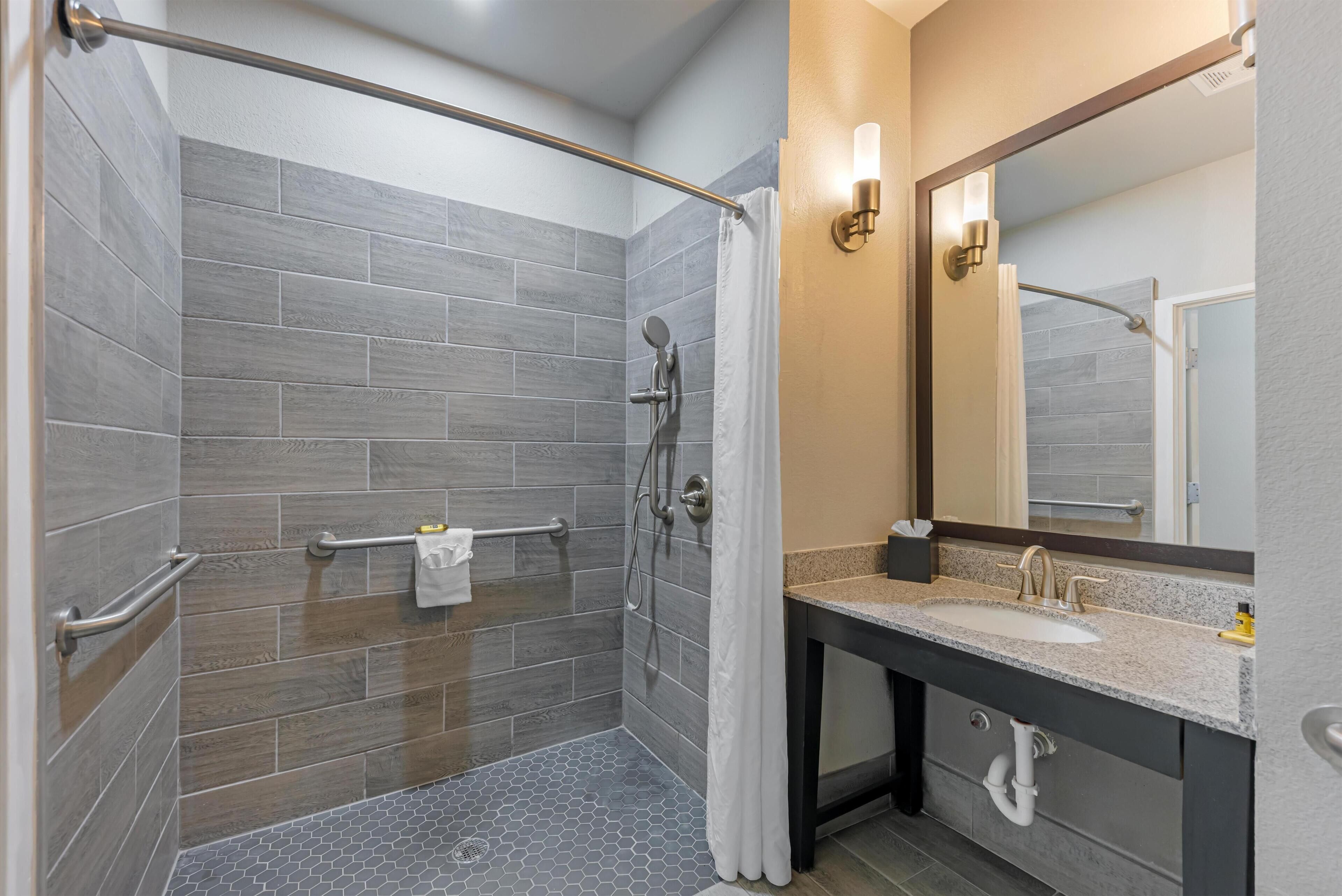 A modern bathroom with a shower, grab bar, and vanity with a sink and mirror.