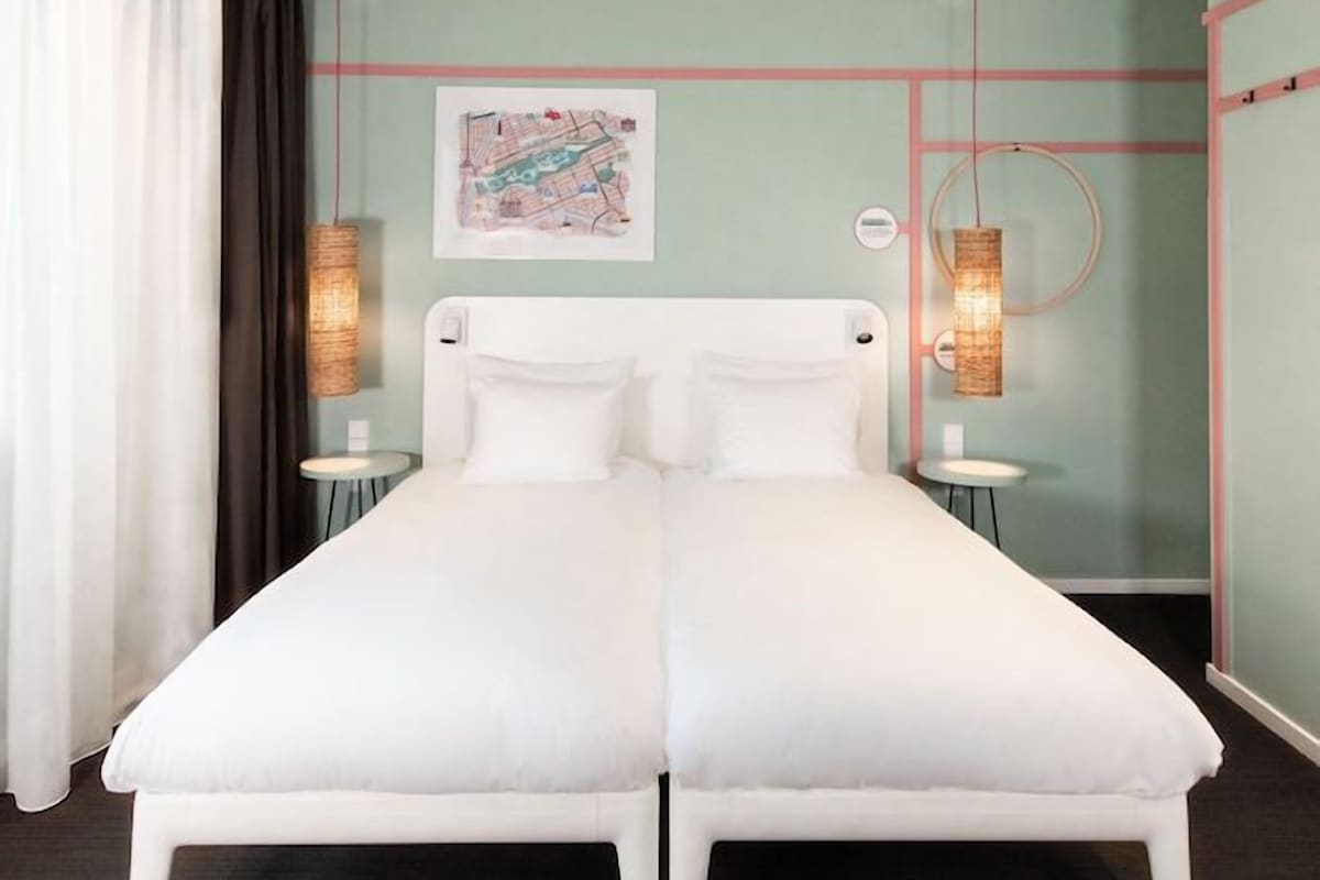 A double bed with white bedding, two bedside tables, a wall map, and a hanging light fixture.