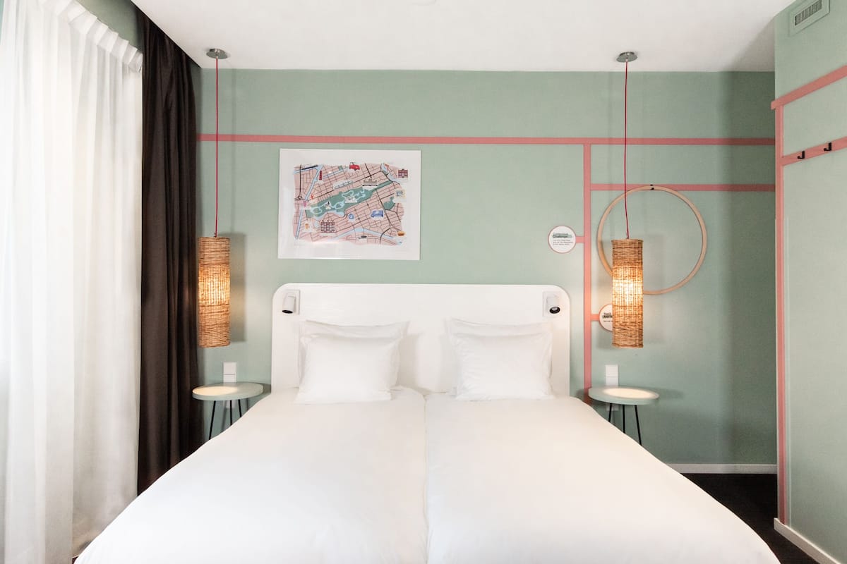A double bed in a room with a green wall, a map, and two bedside lamps.
