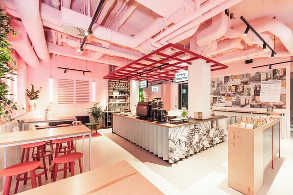A modern bar area with a central counter, bar stools, and a decorative wall with a poster. - Conscious Hotel Vondelpark (Amsterdam)