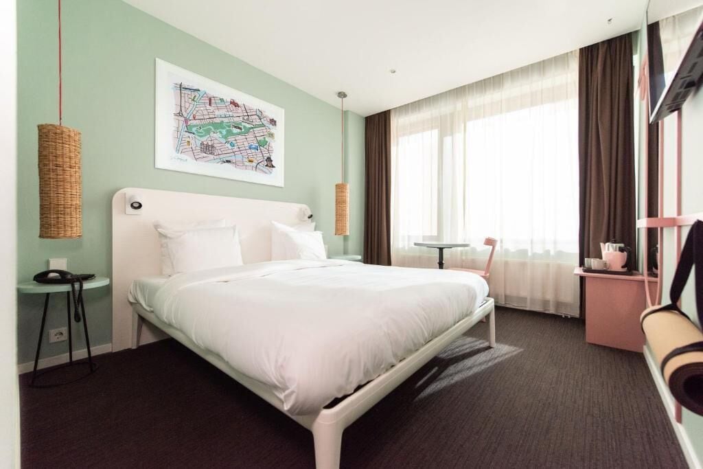 A hotel room with a bed, a map artwork, a small table, a chair, and a television.
