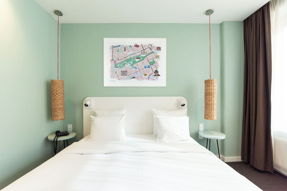 A hotel room with a bed, two bedside tables, a wall-mounted artwork, and a hanging light fixture.