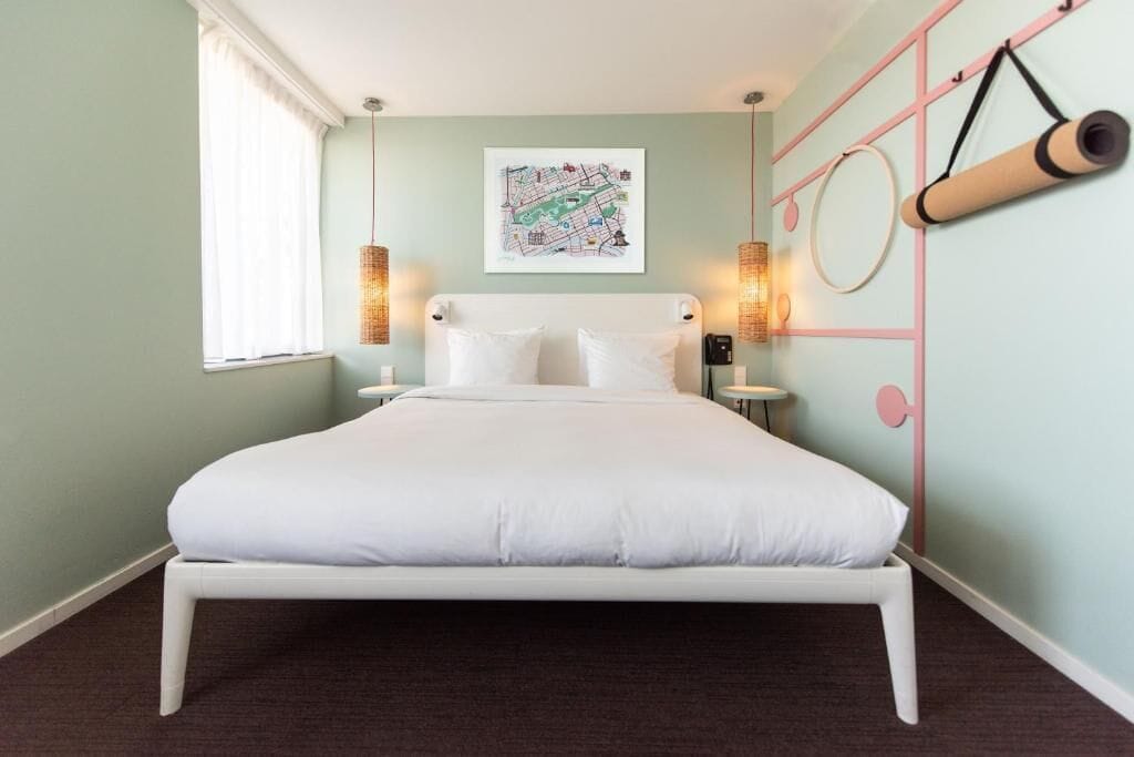 A neatly made bed in a room with a map on the wall, a yoga mat, and a wall-mounted circular object.