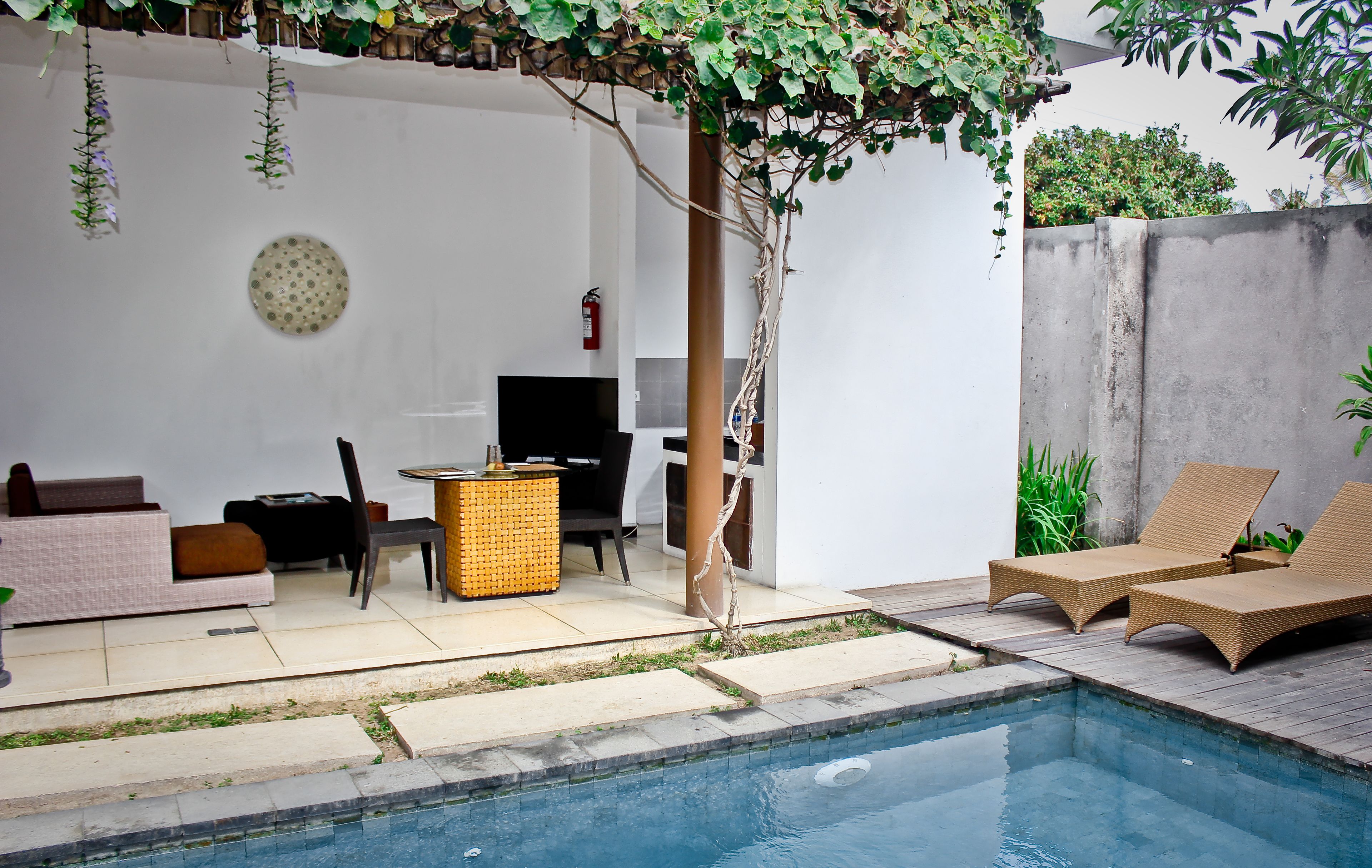 A poolside area with a sofa, chairs, a small table, and lounge chairs.