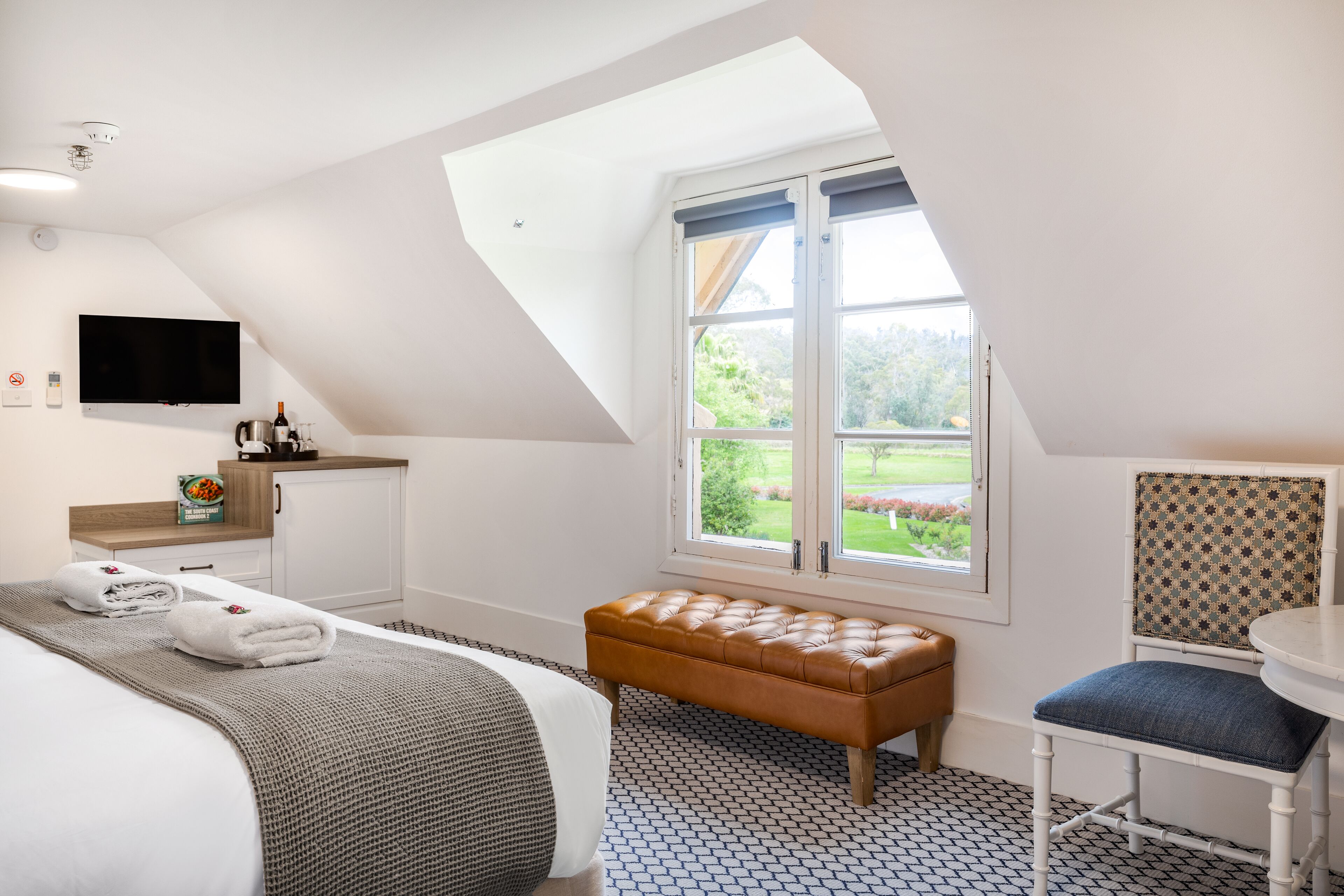 Un dormitorio con cama, un banco, una silla, un televisor y una ventana con vistas a zonas verdes.
